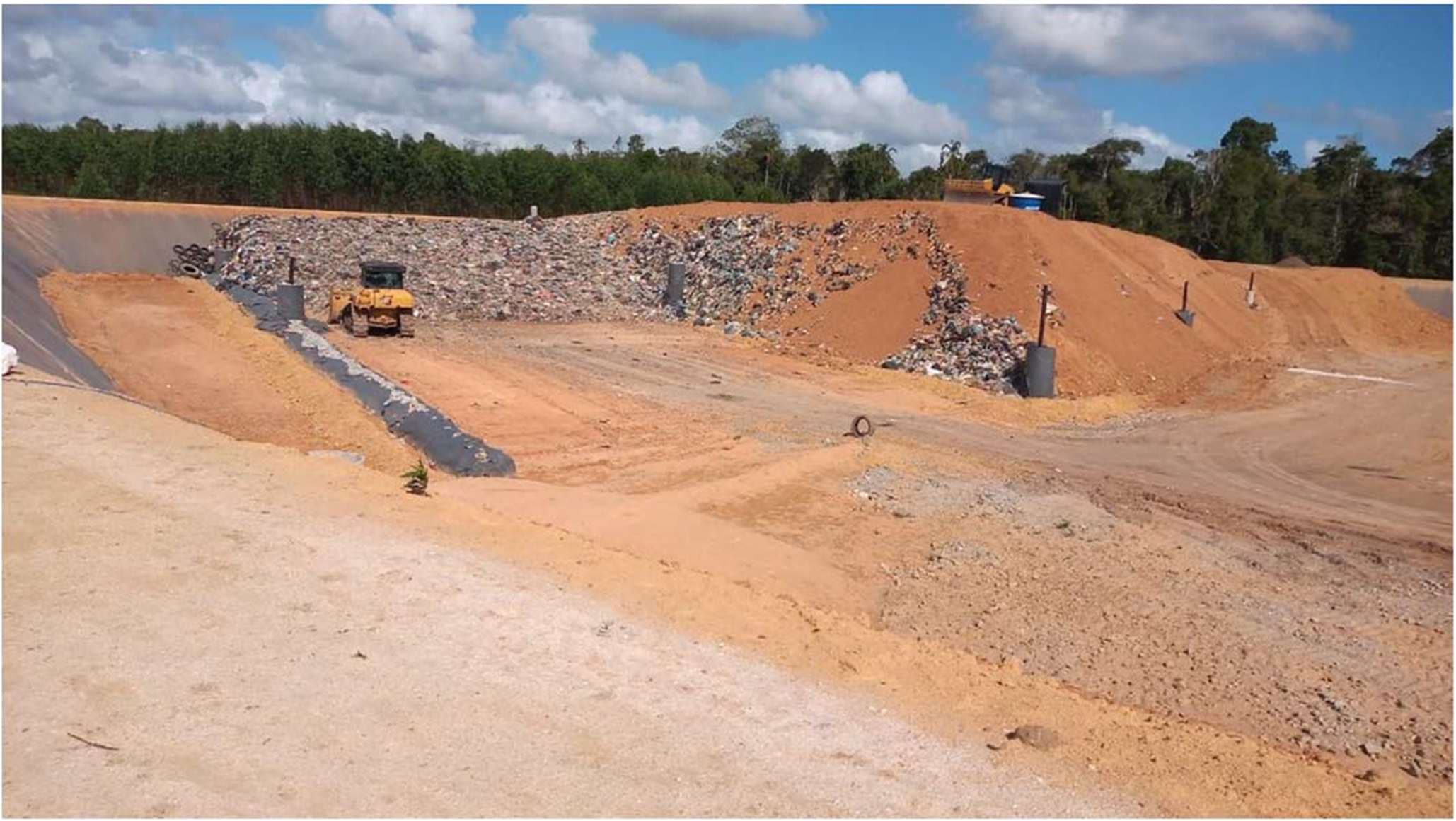Trator compactando resíduos na frente de operação de um aterro sanitário, entre taludes de solo