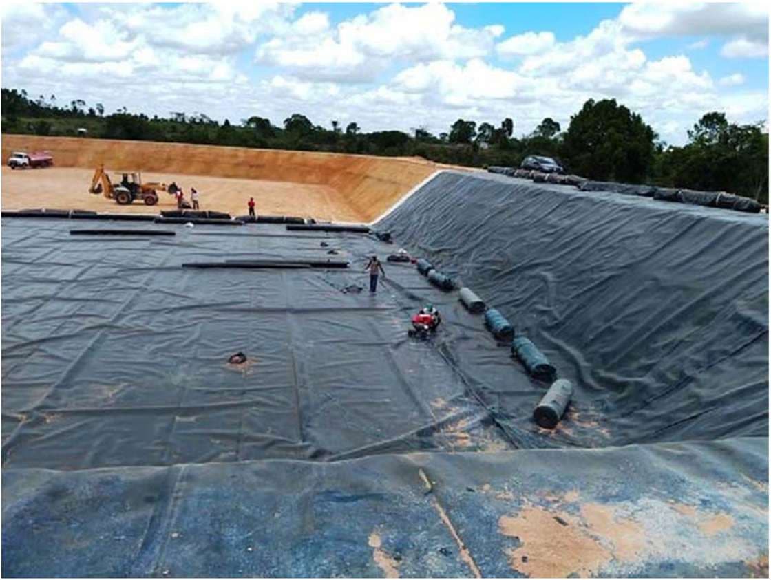 Instalação de geomembrana de impermeabilização em célula de aterro sanitário, com trator e equipe em campo