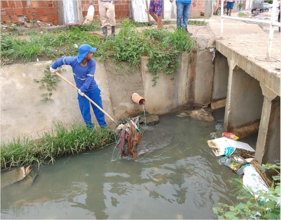 Agente de limpeza retirando resíduos de um canal de drenagem a céu aberto